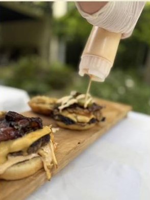 Salsa de la casa sirviéndose sobre hamburguesas recién armadas en una tabla de madera.