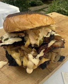 Hamburguesa recién armada con cebolla caramelizada y salsa sobre una tabla de madera.