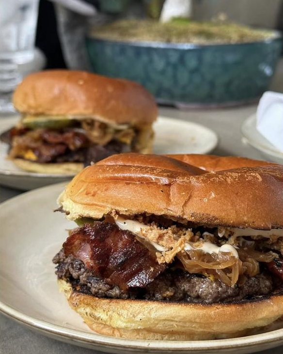 Hamburguesa smash con queso, tocino y cebolla crispy servida en un plato durante un evento.