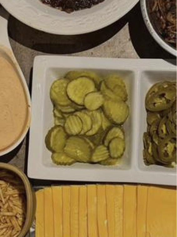 Bandejas con pepinillos, jalapeños, cebolla crispy, queso en láminas y salsa de la casa preparadas para el servicio.